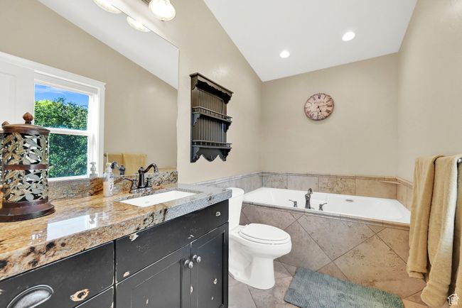 Bathroom with vaulted ceiling, vanity, a relaxing tiled tub, toilet, and tile patterned floors | Image 45