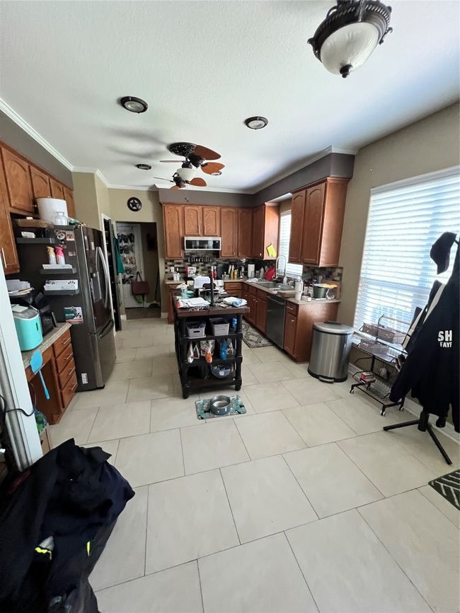 Kitchen featuring tasteful backsplash, dishwashing machine, ceiling fan, ornamental molding, and a kitchen island | Image 10