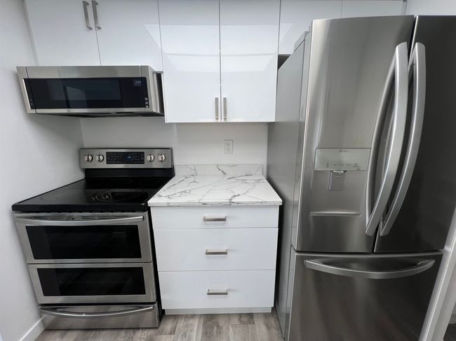 Kitchen featuring appliances with stainless steel finishes, white cabinetry, modern cabinets, light stone counters, and light wood-style floors | Image 12