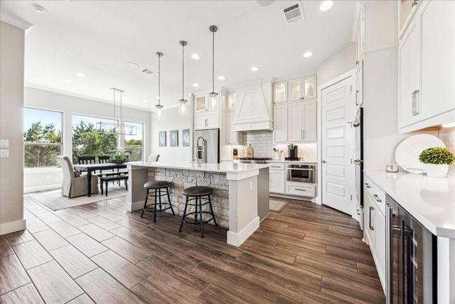 A trio of fashionable pendant lights gracefully accent the kitchen island with quartz countertops, complemented by a striking stone back wall beneath. The oversized island is sure to become a favorite gathering spot in the house hosting homework, to snacks to a causal sit down meal. | Image 13