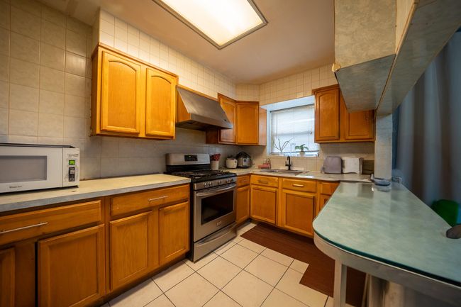 Kitchen featuring range hood, gas range, white microwave, a sink, and light countertops | Image 15