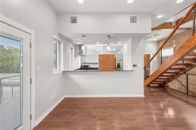 Kitchen with stainless steel fridge with ice dispenser, wall chimney range hood, wood finished floors, recessed lighting, and dark countertops | Image 11