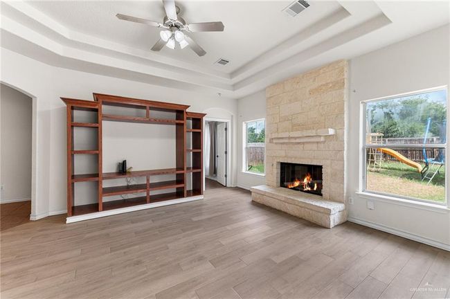 Unfurnished living room with a raised ceiling, arched walkways, a stone fireplace, light wood finished floors, and a ceiling fan | Image 17