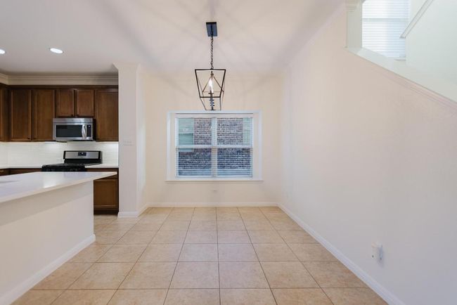 Kitchen featuring light tile patterned floors, decorative backsplash, light countertops, appliances with stainless steel finishes, and decorative light fixtures | Image 10