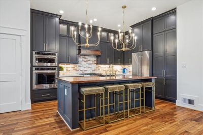 Experience culinary elegance with bespoke cabinetry, sleek stainless steel appliances, a brick backsplash reminiscent of Old Chicago, a charming butcher block island, and chic vintage-inspired gold chandeliers. Refrigerator included for your convenience. | Image 1