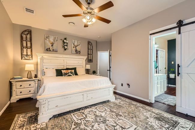 Bedroom featuring dark wood-type flooring, a barn door, and ceiling fan | Image 11