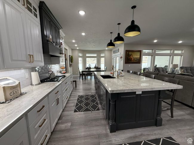 Kitchen with an island with sink, backsplash, a sink, wood finished floors, and stainless steel gas stovetop | Image 22