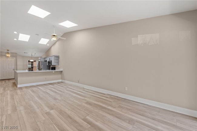 Unfurnished living room with light wood-style flooring, high vaulted ceiling, a ceiling fan, a skylight, and recessed lighting | Image 7