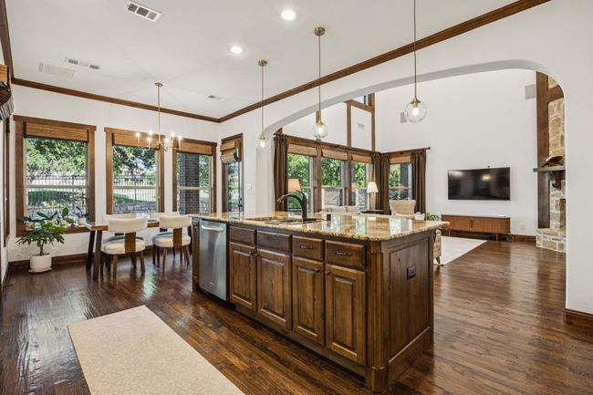 Kitchen featuring stainless steel dishwasher, arched walkways, light stone counters, crown molding, and dark wood-style flooring | Image 13