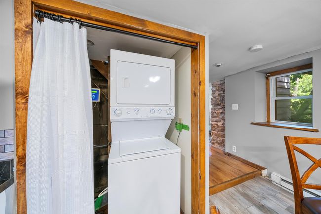 Laundry room with stacked washer / drying machine, wood finished floors, and a baseboard radiator | Image 7