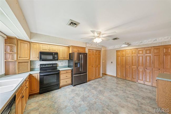 Kitchen with black appliances, ceiling fan, light floors, open shelves, and light countertops | Image 9