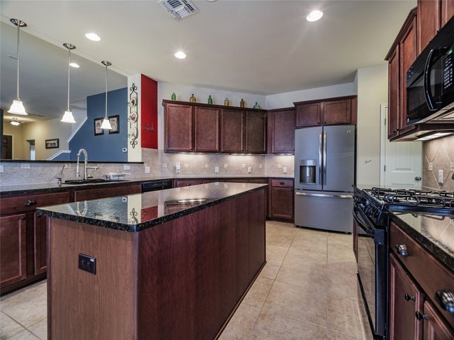 Kitchen featuring black appliances, a sink, a center island, decorative backsplash, and dark stone countertops | Image 18