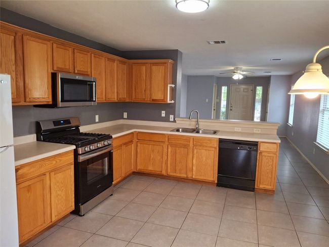 Kitchen featuring new gas stove and microwave appliances, a sink, light countertops, and a ceiling fan | Image 5