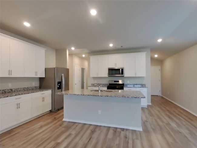 Kitchen featuring appliances with stainless steel finishes, a sink, a kitchen island with sink, light wood-style floors, and white cabinetry | Image 4