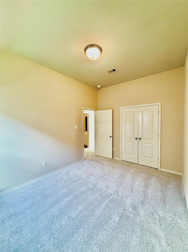 Third bedroom is a carpeted room with neutral walls and ceiling, a light fixture, double closet doors, and a doorway leading to hallway next to second bedroom. | Image 10