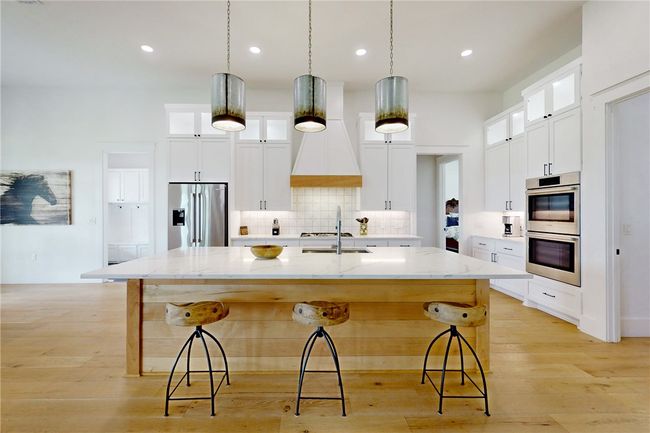 Kitchen with appliances with stainless steel finishes, a large island with sink, decorative backsplash, a kitchen breakfast bar, and light wood finished floors | Image 8