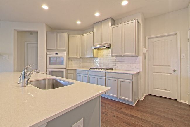 Kitchen featuring white double oven, stainless steel gas stovetop, dark wood-type flooring, light countertops, and tasteful backsplash | Image 14