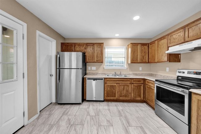 Kitchen with light countertops, brown cabinets, stainless steel appliances, under cabinet range hood, and a sink | Image 7