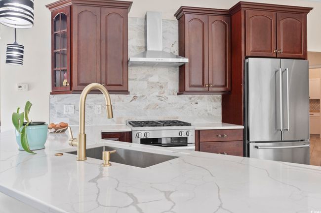 Kitchen with appliances with stainless steel finishes, wall chimney range hood, a sink, light stone countertops, and backsplash | Image 7