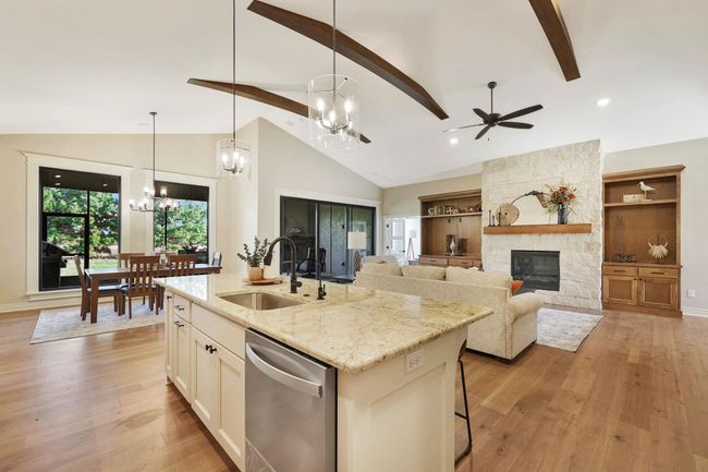 Kitchen featuring light stone counters, a kitchen island with sink, ceiling fan with notable chandelier, a fireplace, and stainless steel dishwasher | Image 10