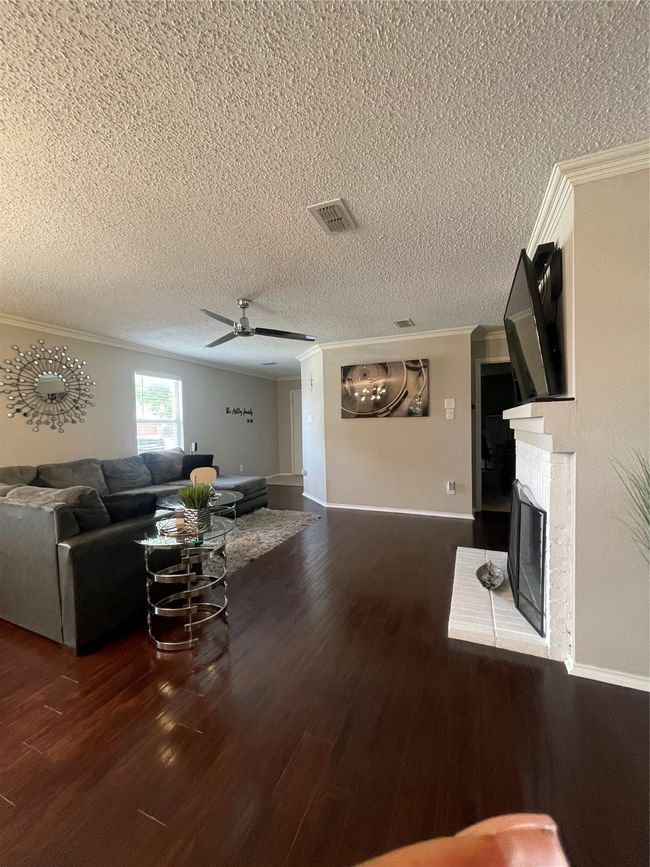 Living area with crown molding, a fireplace, wood finished floors, a ceiling fan, and a textured ceiling | Image 9