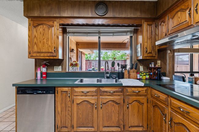 Kitchen featuring black electric cooktop, dishwasher, light tile patterned floors, a sink, and brown cabinetry | Image 29