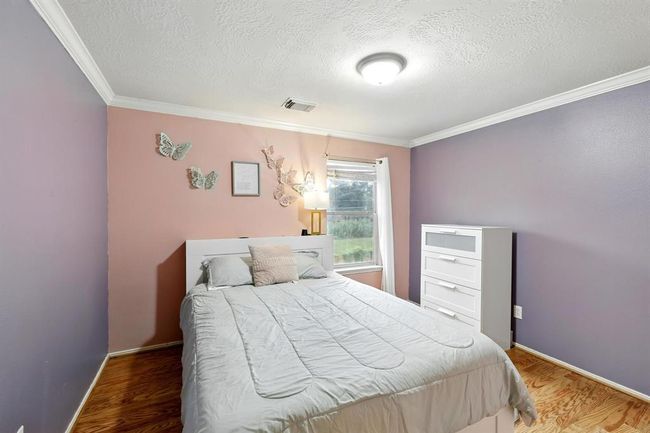 Charming secondary bedroom with crown molding, warm wood flooring, and soft accent walls, offering a cozy and colorful retreat. | Image 19