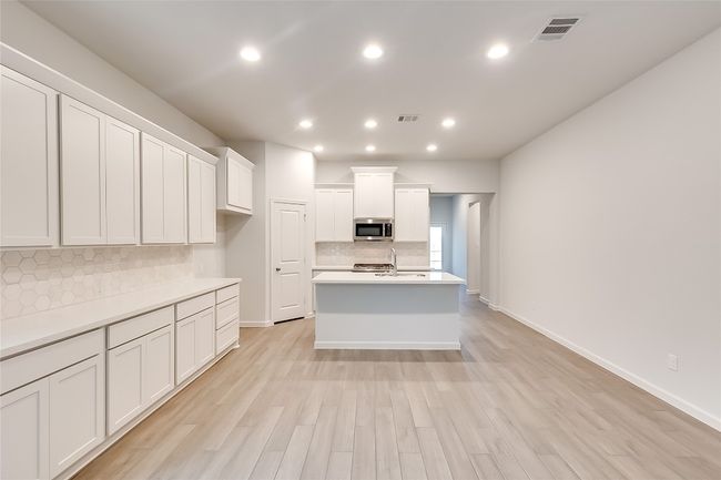 Kitchen with stainless steel microwave, tasteful backsplash, white cabinetry, light countertops, and light wood finished floors | Image 9