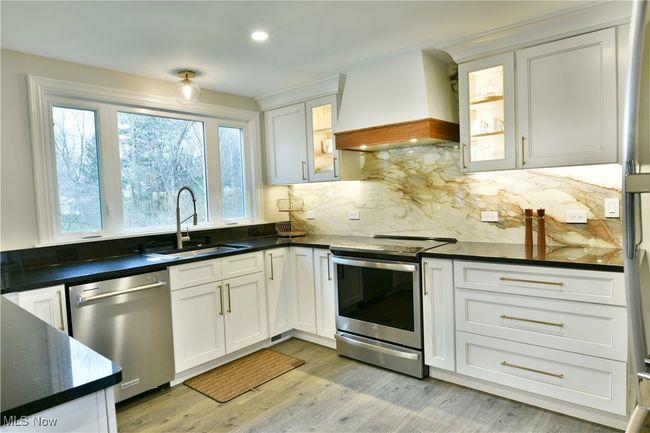 Kitchen with custom exhaust hood, appliances with stainless steel finishes, dark countertops, and a sink | Image 17