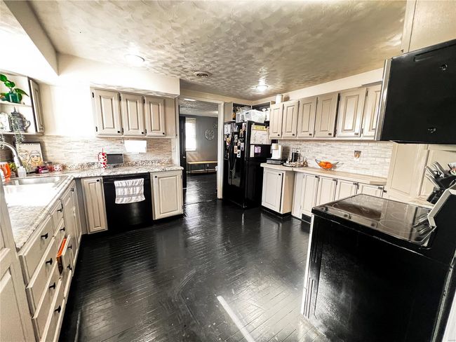 Kitchen with dark wood-style floors, light countertops, a sink, and black appliances | Image 20