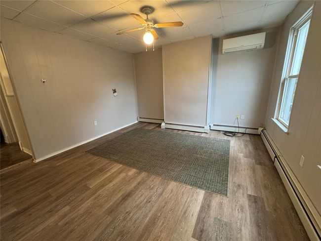 Spare room featuring a wall mounted AC, dark wood-style floors, baseboard heating, a drop ceiling, and a ceiling fan | Image 5