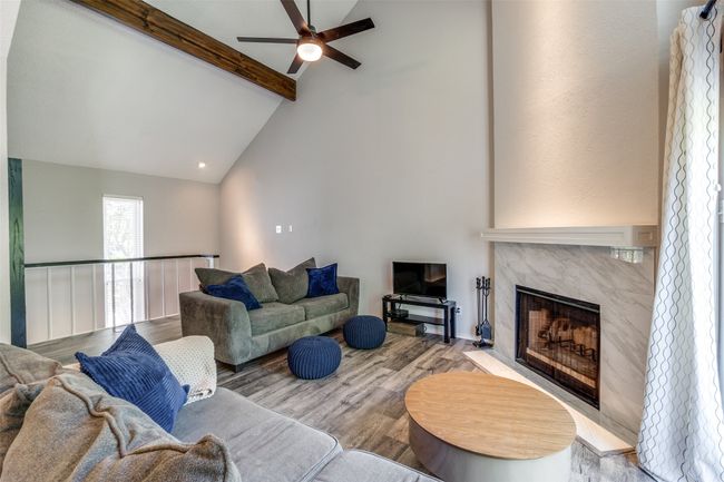 Living area featuring a ceiling fan, beamed ceiling, a tiled fireplace, wood finished floors, and high vaulted ceiling | Image 16