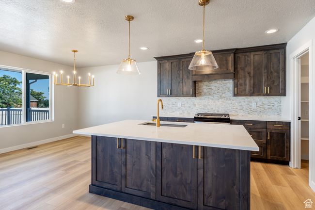 Kitchen with black electric range oven, backsplash, light wood-type flooring, dark brown cabinetry, and a textured ceiling | Image 9