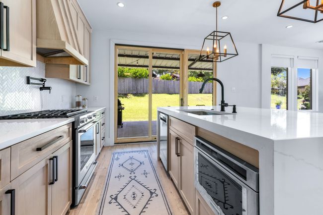 Kitchen featuring custom exhaust hood, appliances with stainless steel finishes, tasteful backsplash, light wood-style floors, and a chandelier.....Dont forget the patio and pool are just outside the sliding door. | Image 16