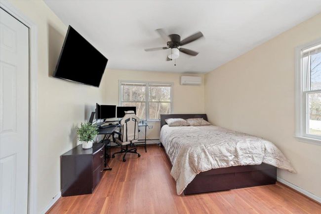 Bedroom with wood finished floors, an AC wall unit, baseboards, ceiling fan, and baseboard heating | Image 14
