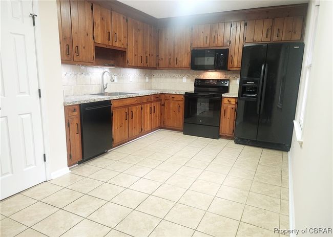 Kitchen featuring sink, light tile patterned floors, backsplash, and black appliances | Image 5