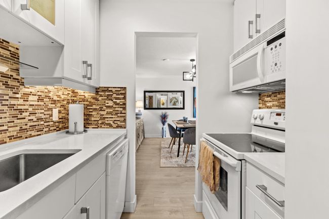 Kitchen featuring light wood-style flooring, backsplash, white appliances, white cabinets, and light countertops | Image 11