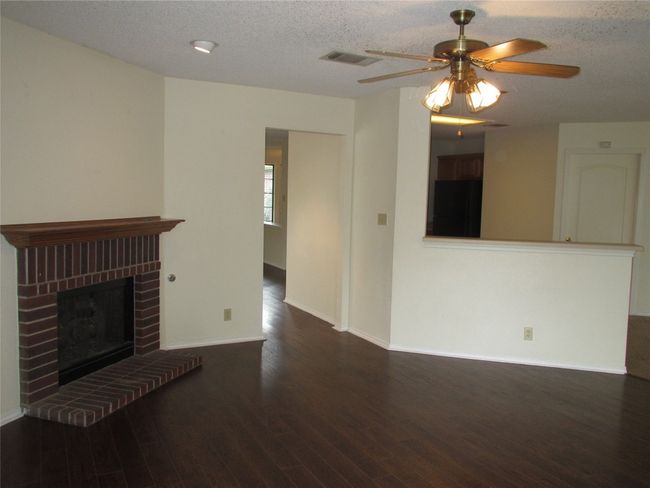 Unfurnished living room featuring a textured ceiling, a fireplace, dark wood-type flooring, and a ceiling fan | Image 4