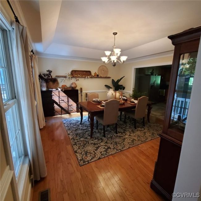 Dining room with visible vents, crown molding, a tray ceiling, an inviting chandelier, and wood finished floors | Image 14