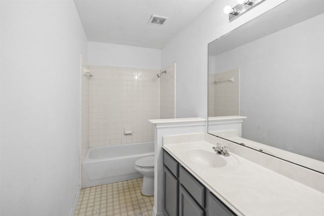 Full bathroom featuring washtub / shower combination, vanity, toilet, tile patterned floors, and visible vents | Image 24