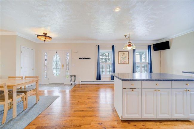 Kitchen featuring light wood-style floors, ornamental molding, white cabinetry, a baseboard heating unit, and dark countertops | Image 12