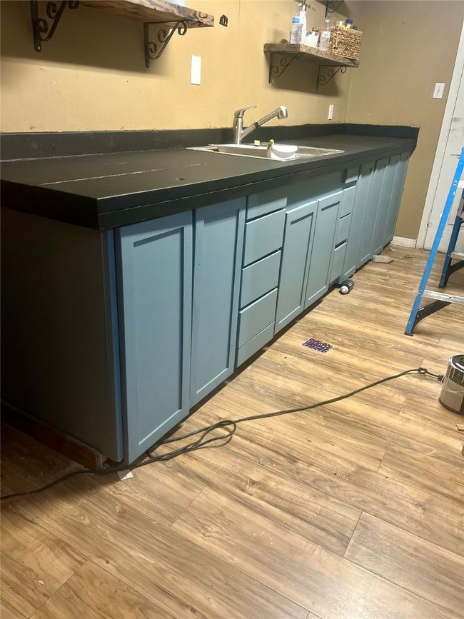 Kitchen with dark countertops, light wood-style flooring, blue cabinets, and open shelves | Image 5