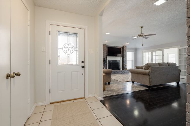Entrance foyer featuring a textured ceiling, ceiling fan, light tile patterned floors, a fireplace, and baseboards | Image 5