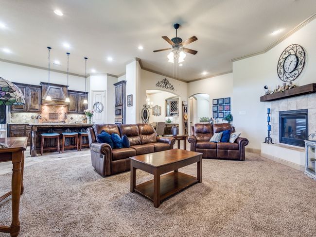 Living room with arched walkways, light colored carpet, ornamental molding, ceiling fan, and a tiled fireplace | Image 8