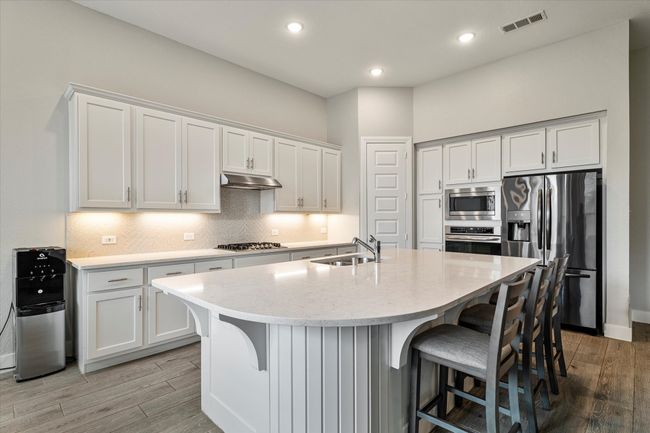 Kitchen featuring light wood finished floors, appliances with stainless steel finishes, under cabinet range hood, and a kitchen bar | Image 8