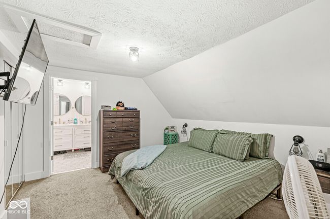carpeted bedroom with connected bathroom, vaulted ceiling, and a textured ceiling | Image 18