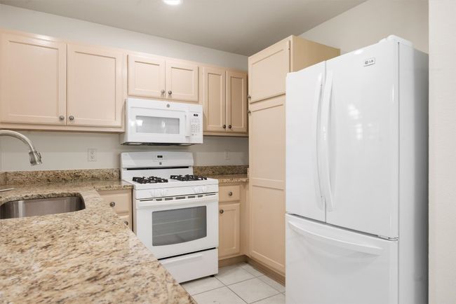 Kitchen featuring white appliances, light tile patterned floors, and light stone counters | Image 20