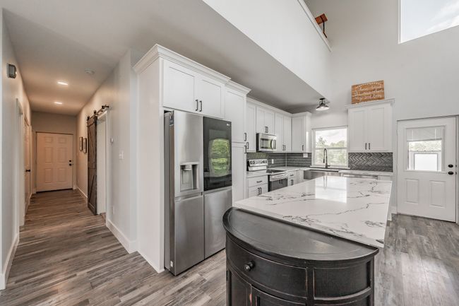 Kitchen featuring appliances with stainless steel finishes, wood finished floors, white cabinets, decorative backsplash, and a barn door | Image 24