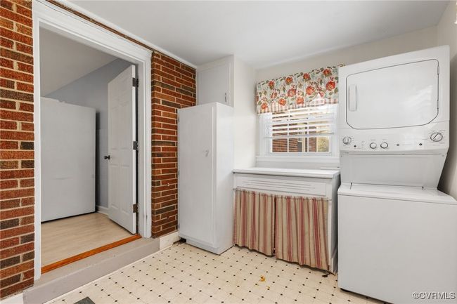 Washroom featuring stacked washer and dryer, brick wall, and light floors | Image 24