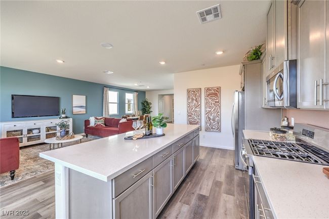 Kitchen with stainless steel appliances, open floor plan, gray cabinets, light countertops, and light wood finished floors. Photo is representational only; actual home finishes may vary. | Image 15